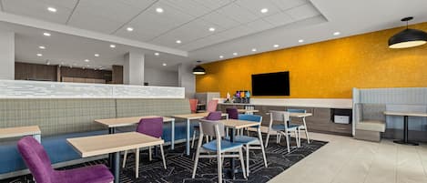 Un restaurant moderne avec des banquettes et des tables, un mur d’accent jaune et un plafond noir.