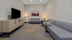 A modern hotel room with a flat-screen TV, grey sofa, and a patterned carpet. - Home2 Suites By Hilton Lebanon (Lebanon)