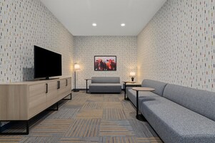 A modern hotel room with a flat-screen TV, grey sofa, and a patterned carpet.