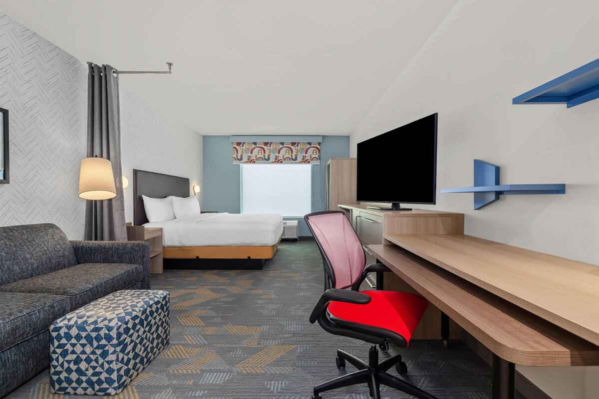 A hotel room with a bed, a desk, a chair, a TV, and a sofa.