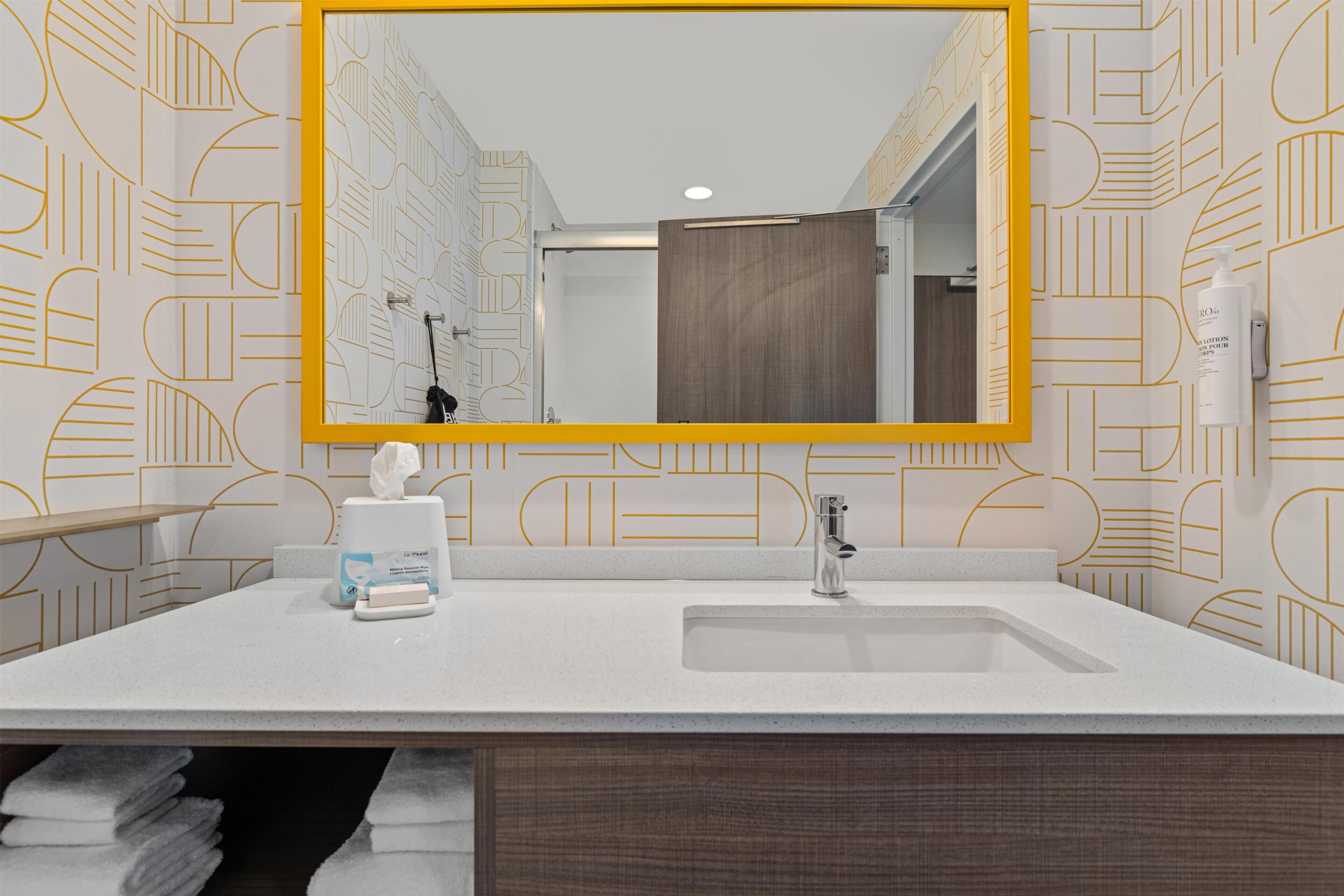 Un bany amb un mirall gran, un lavabo, una barra de tovalloles i un vàter.