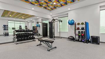 A gym with exercise equipment, a bench, dumbbells, and a ceiling with geometric patterns.