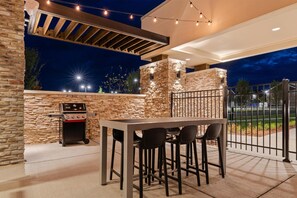An outdoor patio with a stone wall, a barbecue grill, and a table with chairs. - Home2 Suites By Hilton Lebanon (Lebanon)