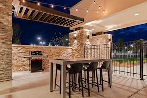 An outdoor patio with a stone wall, a barbecue grill, and a table with chairs.