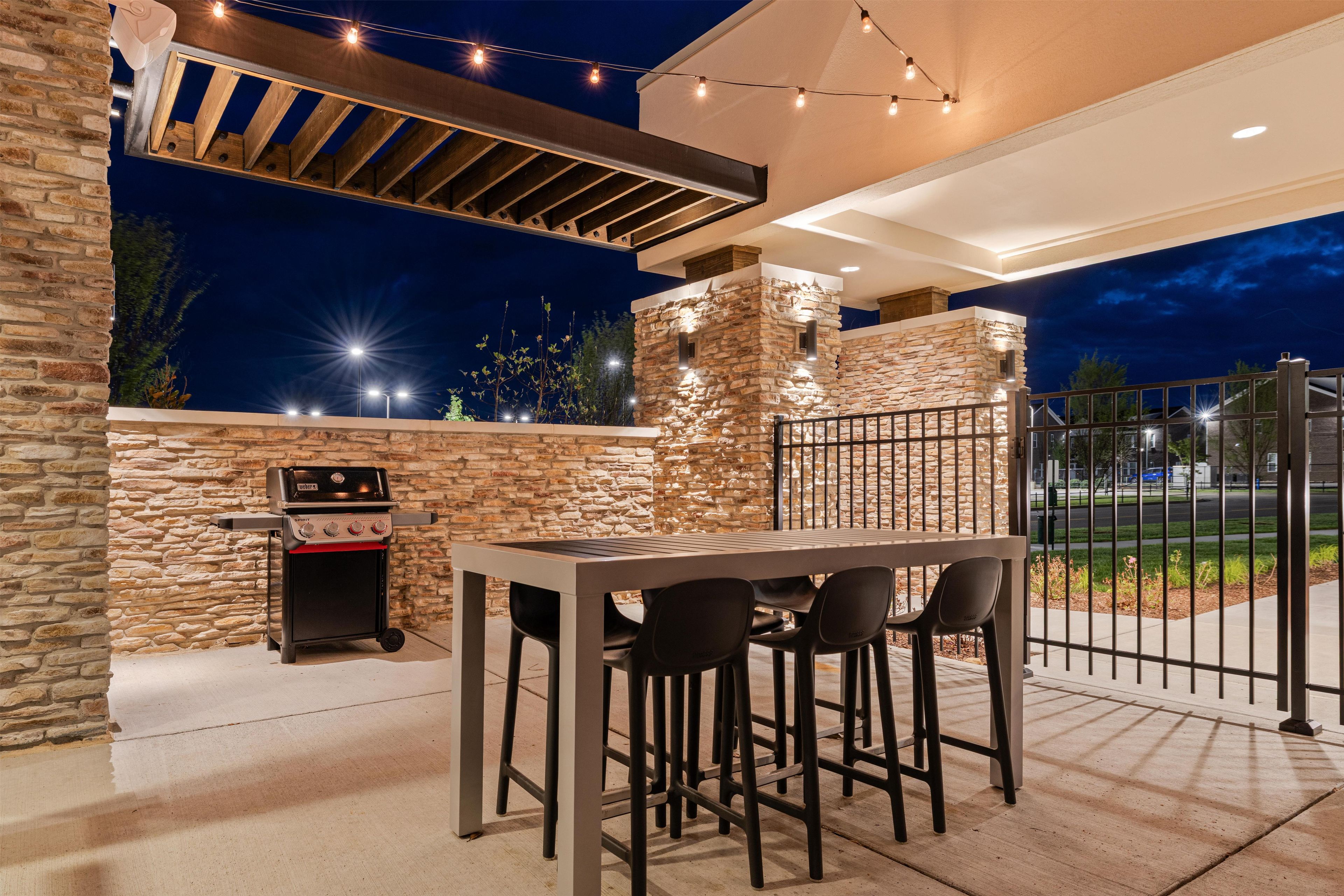 An outdoor patio with a stone wall, a barbecue grill, and a table with chairs.