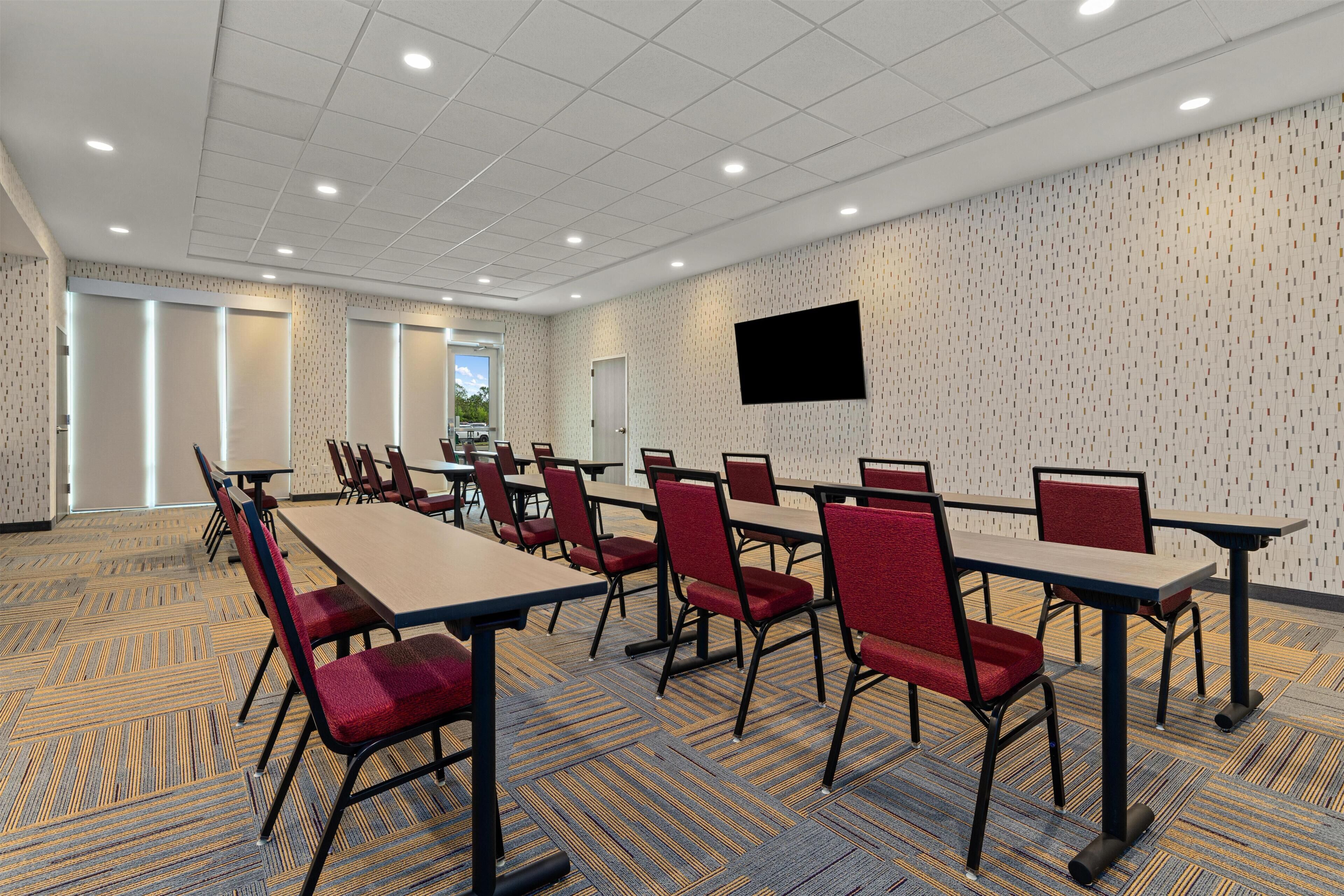 A conference room with tables and chairs, a flat-screen TV, and patterned carpet.