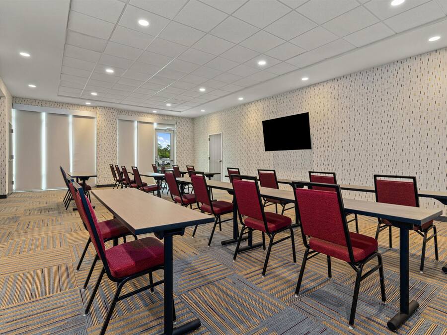 A conference room with tables and chairs, a flat-screen TV, and patterned carpet.