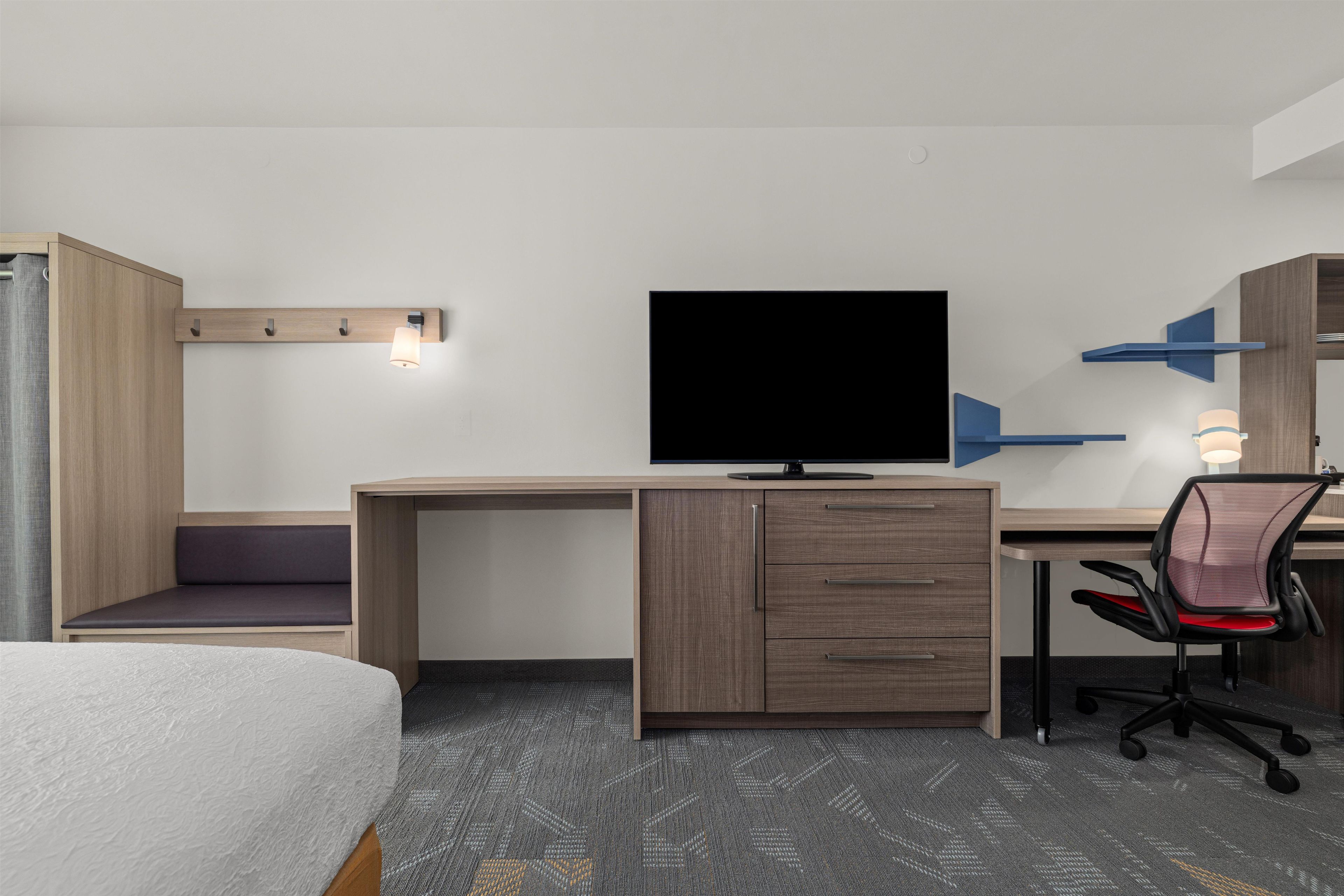 A hotel room with a bed, a desk with a television, a chair, and a wardrobe.