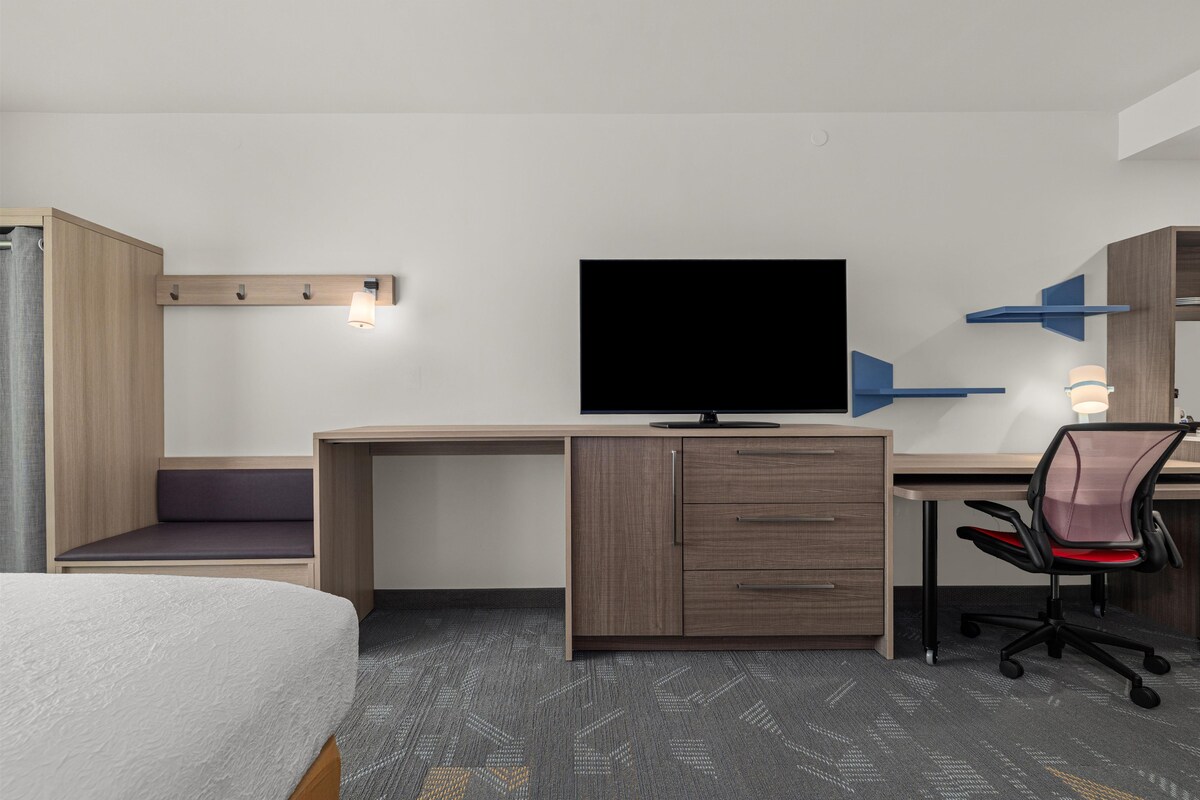 A hotel room with a bed, a desk with a television, a chair, and a wardrobe.