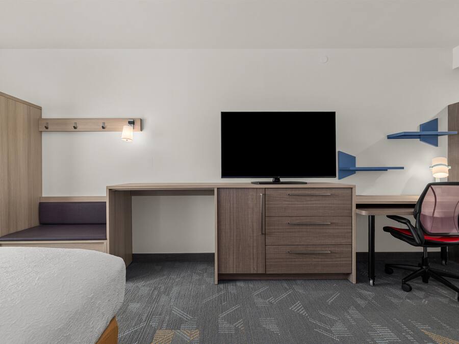 Una habitación de hotel con una cama, un escritorio con televisor, una silla y un armario.