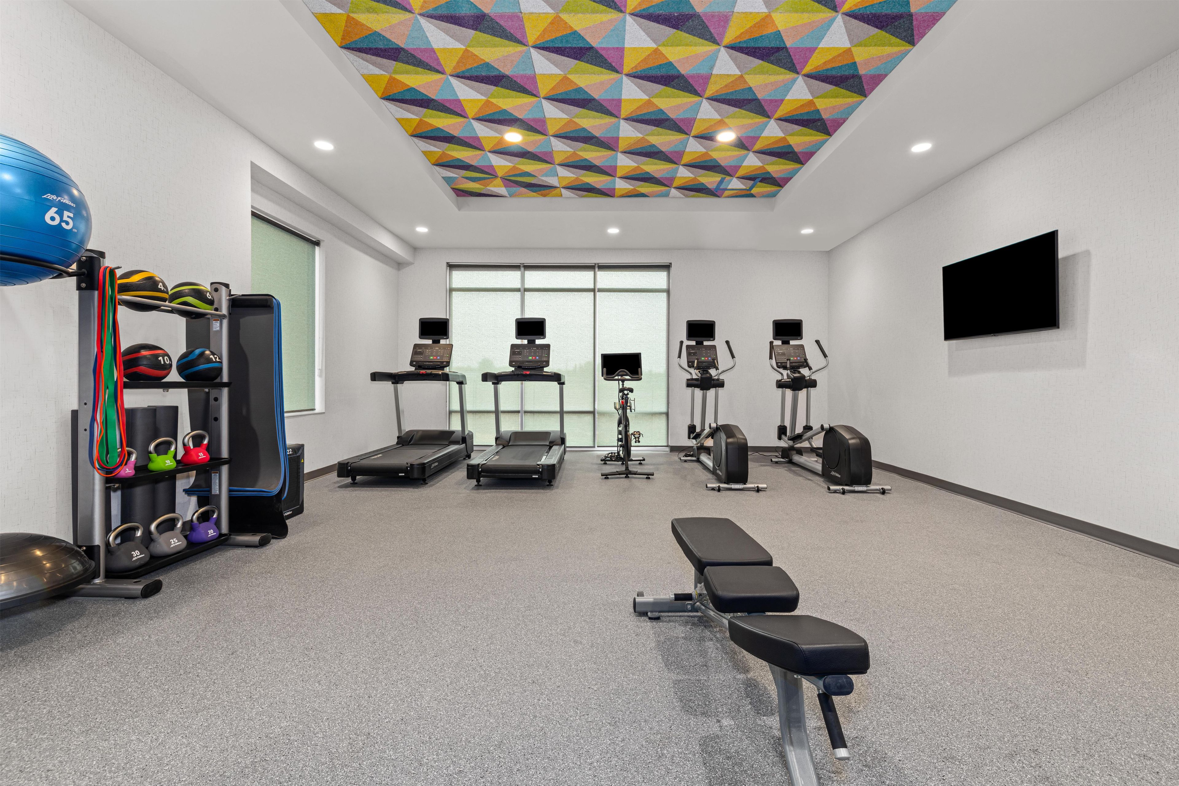 A gym with exercise equipment, a bench, and a colorful geometric ceiling.