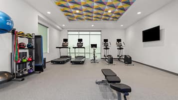 A gym with exercise equipment, a bench, and a colorful geometric ceiling.
