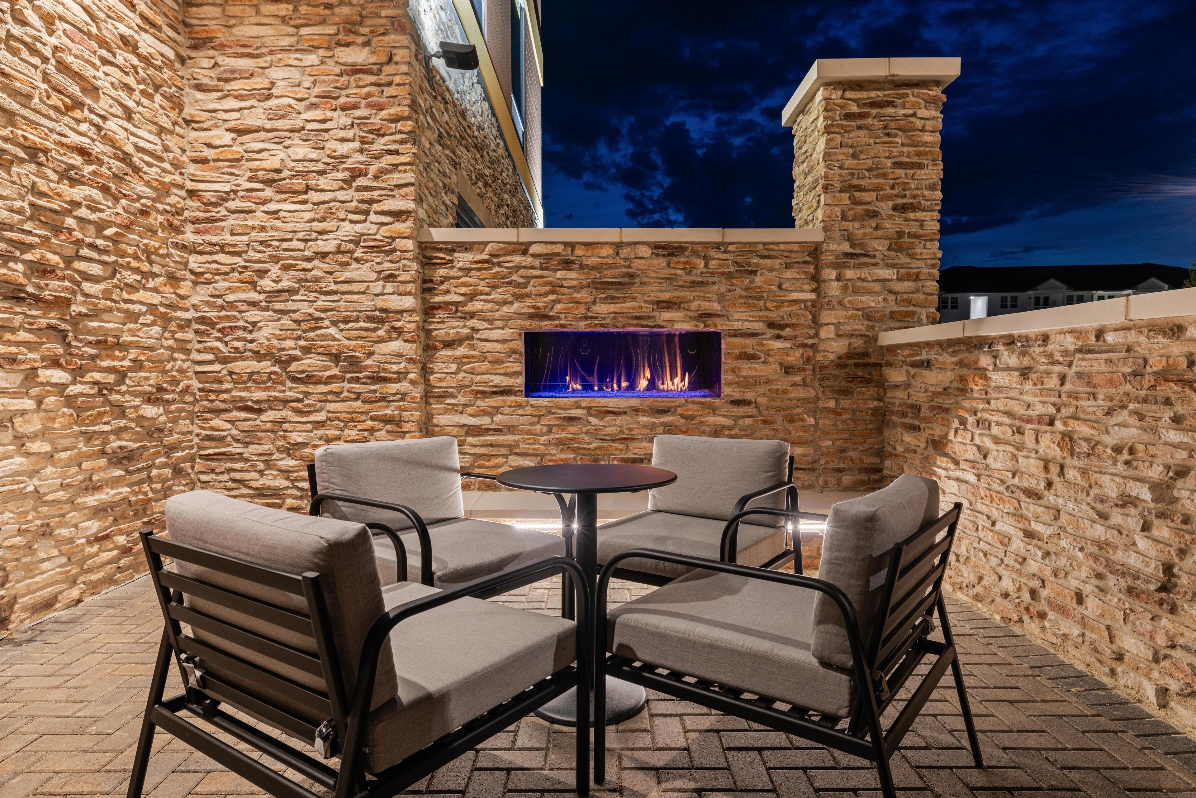 An outdoor patio with stone walls, a fire feature, and four chairs.