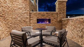An outdoor patio with stone walls, a fire feature, and four chairs.