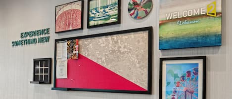 Una pared con varios cuadros enmarcados, incluyendo una noria, un letrero de bienvenida y una obra abstracta roja y beige.