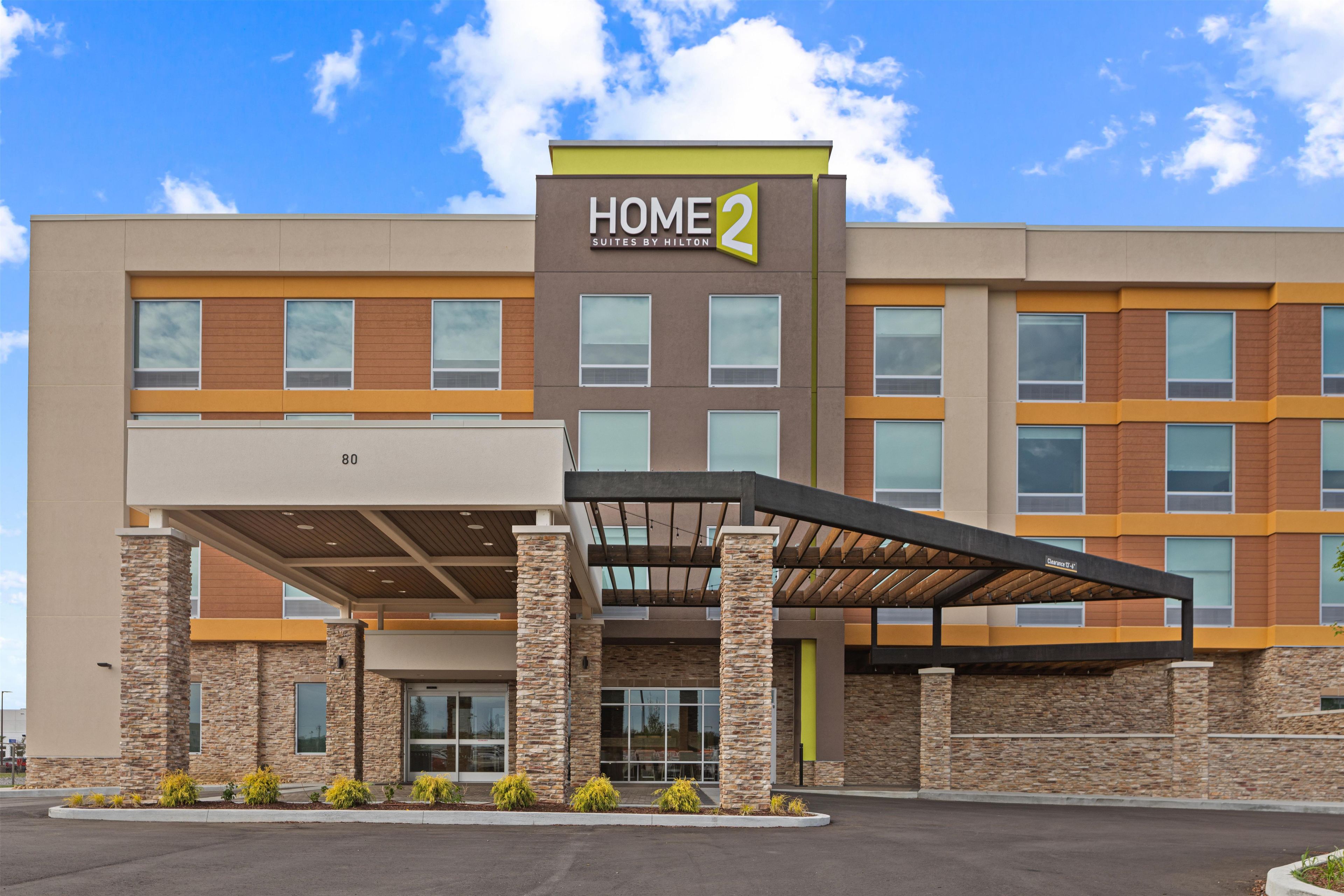A modern hotel building with a 'HOME 2' sign, multiple windows, and a covered entrance area.