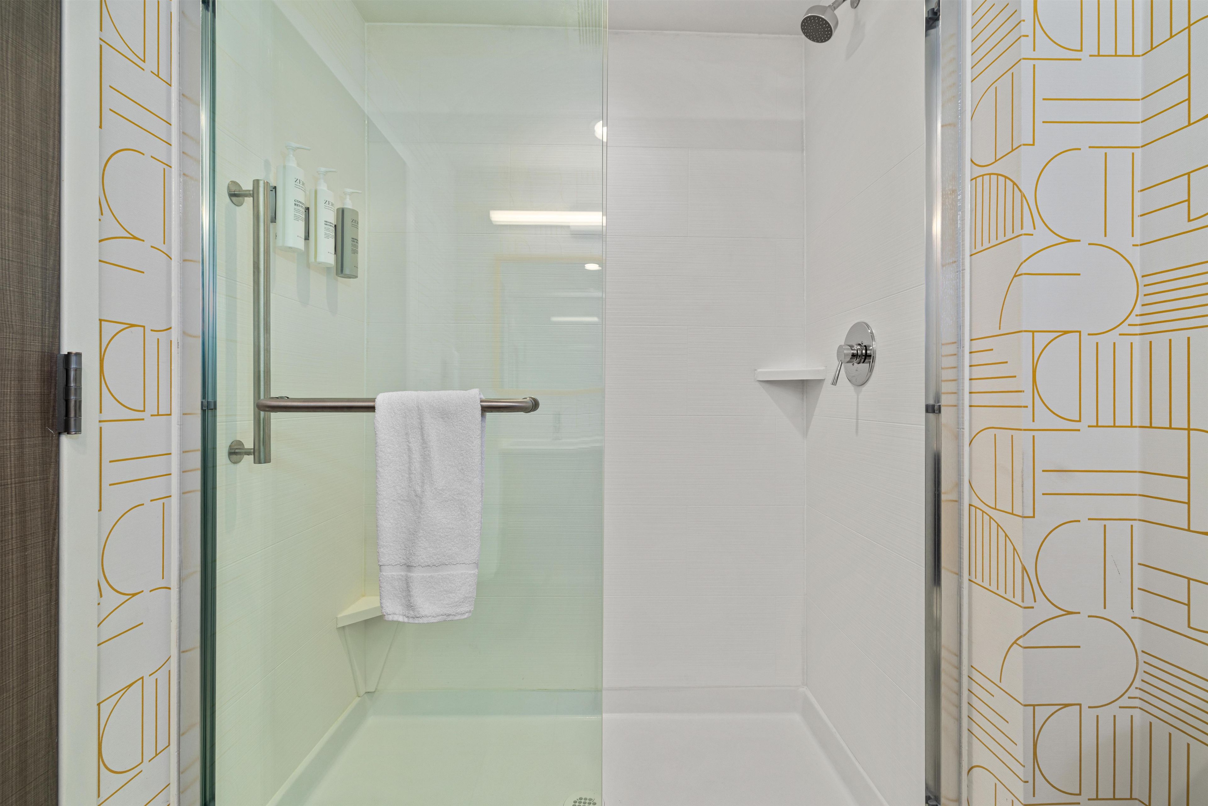 A glass-enclosed shower with a white towel on a rack, a glass door, and a patterned wall design.