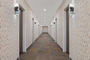 Un pasillo de hotel con paredes estampadas, iluminación empotrada y suelo alfombrado.