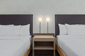 A hotel room with two beds, a nightstand with two wall-mounted lights, and a herringbone-patterned wallpaper.