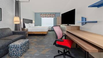 A hotel room with a bed, a desk, a chair, a TV, and a sofa.