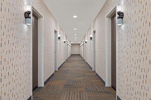 A hotel hallway with patterned walls, recessed lighting, and a carpeted floor. - Home2 Suites By Hilton Lebanon (Lebanon)