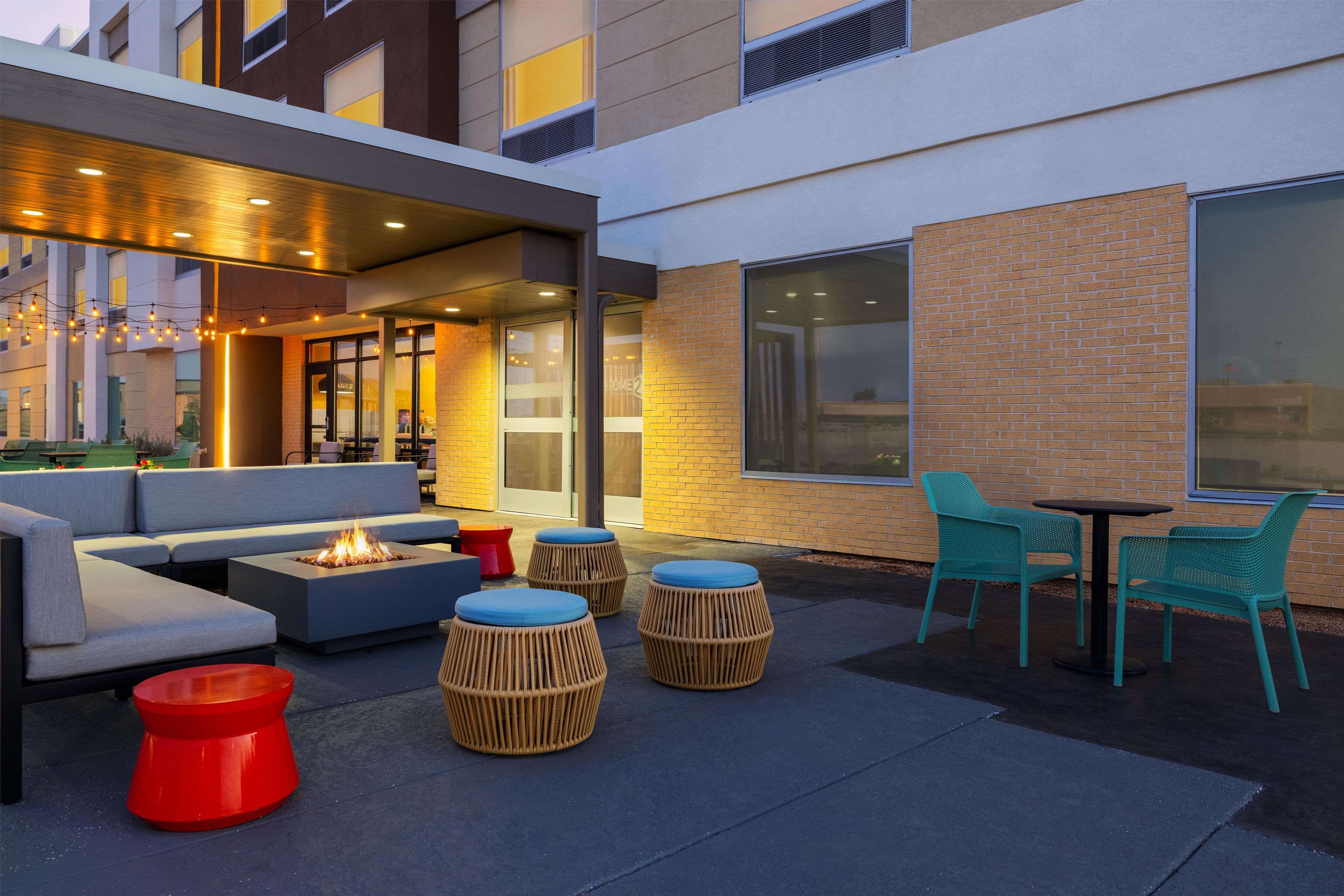 An outdoor seating area with a fire feature, wicker ottomans, and a table with chairs.