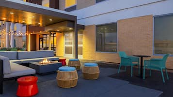An outdoor seating area with a fire feature, wicker ottomans, and a table with chairs.