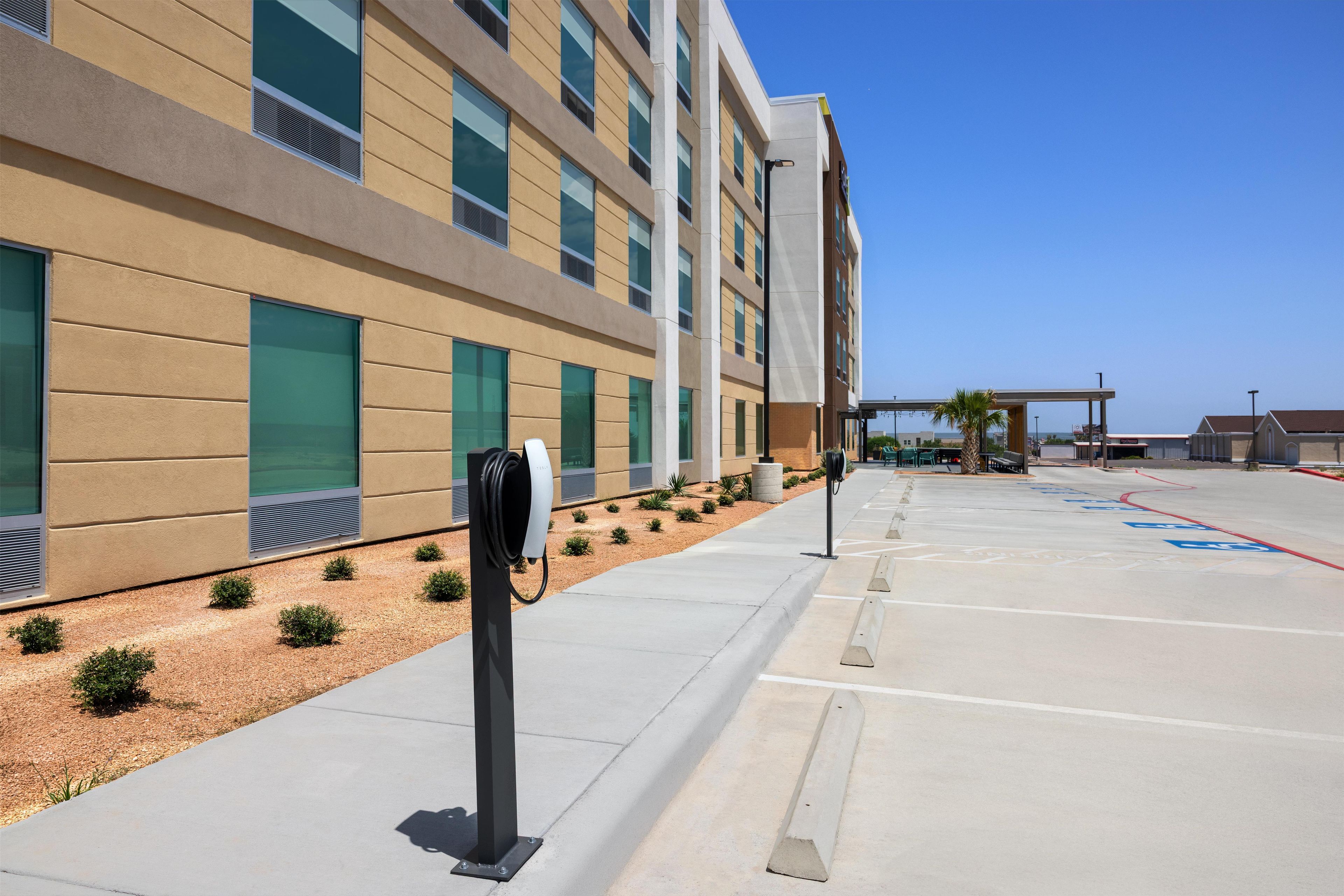 A parking area with electric vehicle charging stations, a clear sky, and a building with large windows and a modern design.