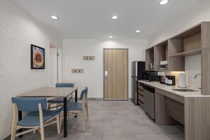 Una cocina moderna con comedor, que presenta una puerta de madera, electrodomésticos integrados y un revestimiento de pared en patrón de espiga.