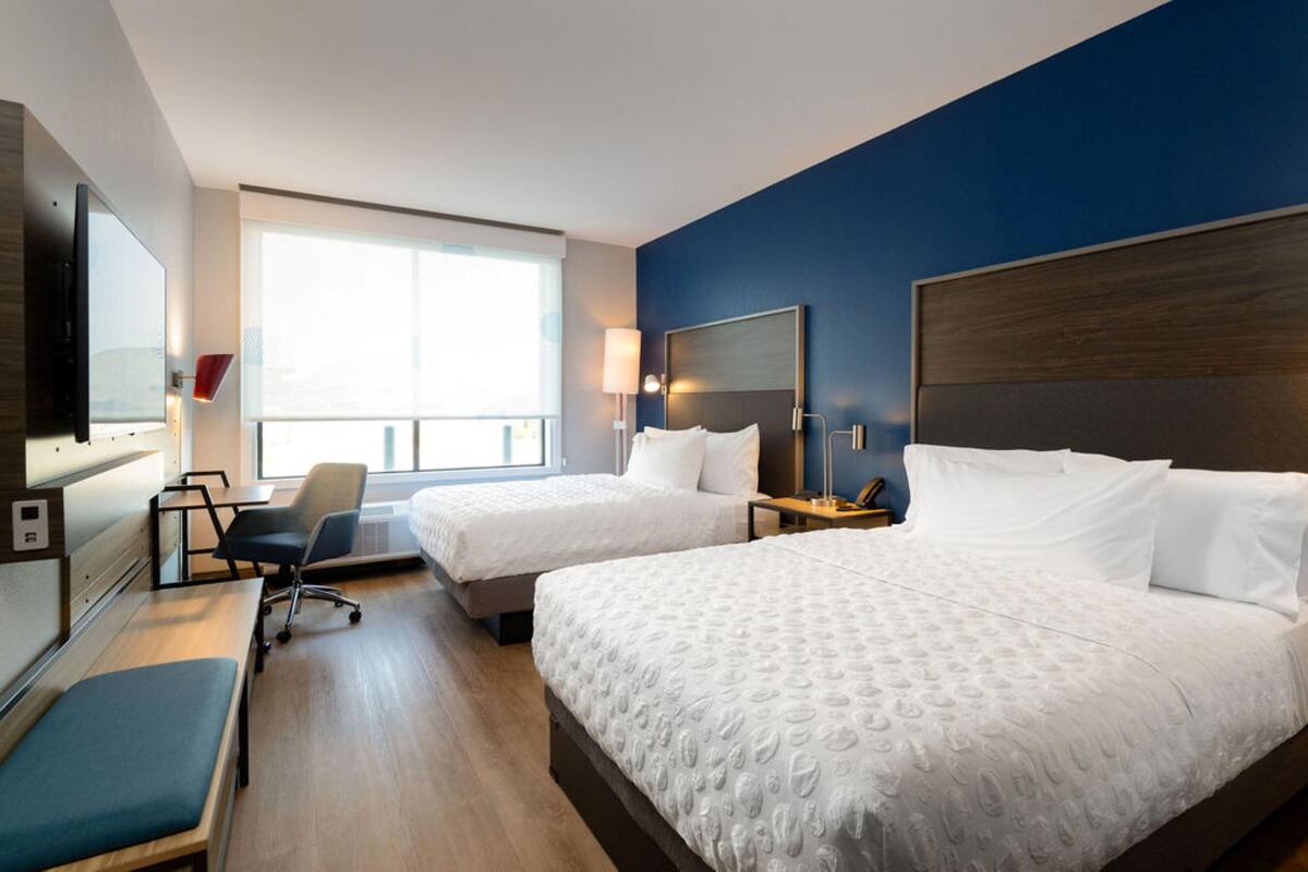 Een hotelkamer met twee bedden, een bureau, een stoel, een televisie en een groot raam.