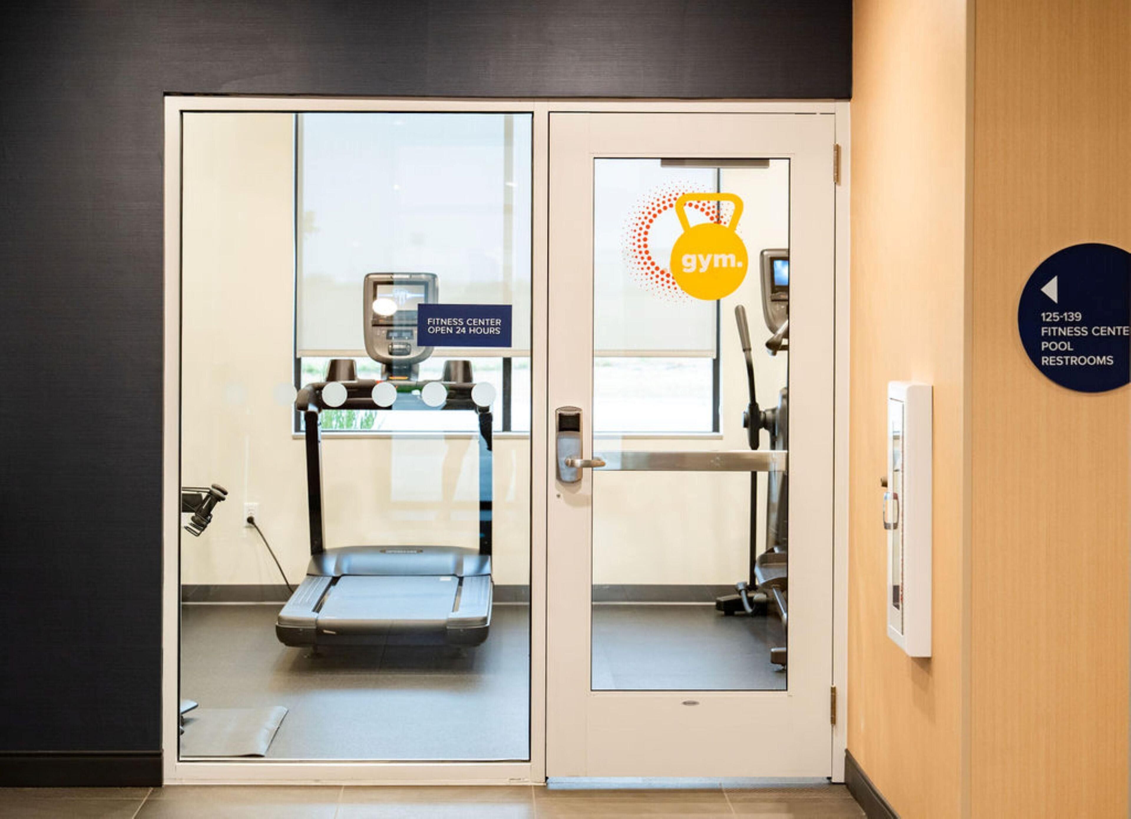 A fitness center with a treadmill, a weight machine, and a sign indicating it's open 24 hours.