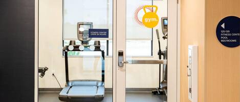 A fitness center with a treadmill, a weight machine, and a sign indicating it's open 24 hours.