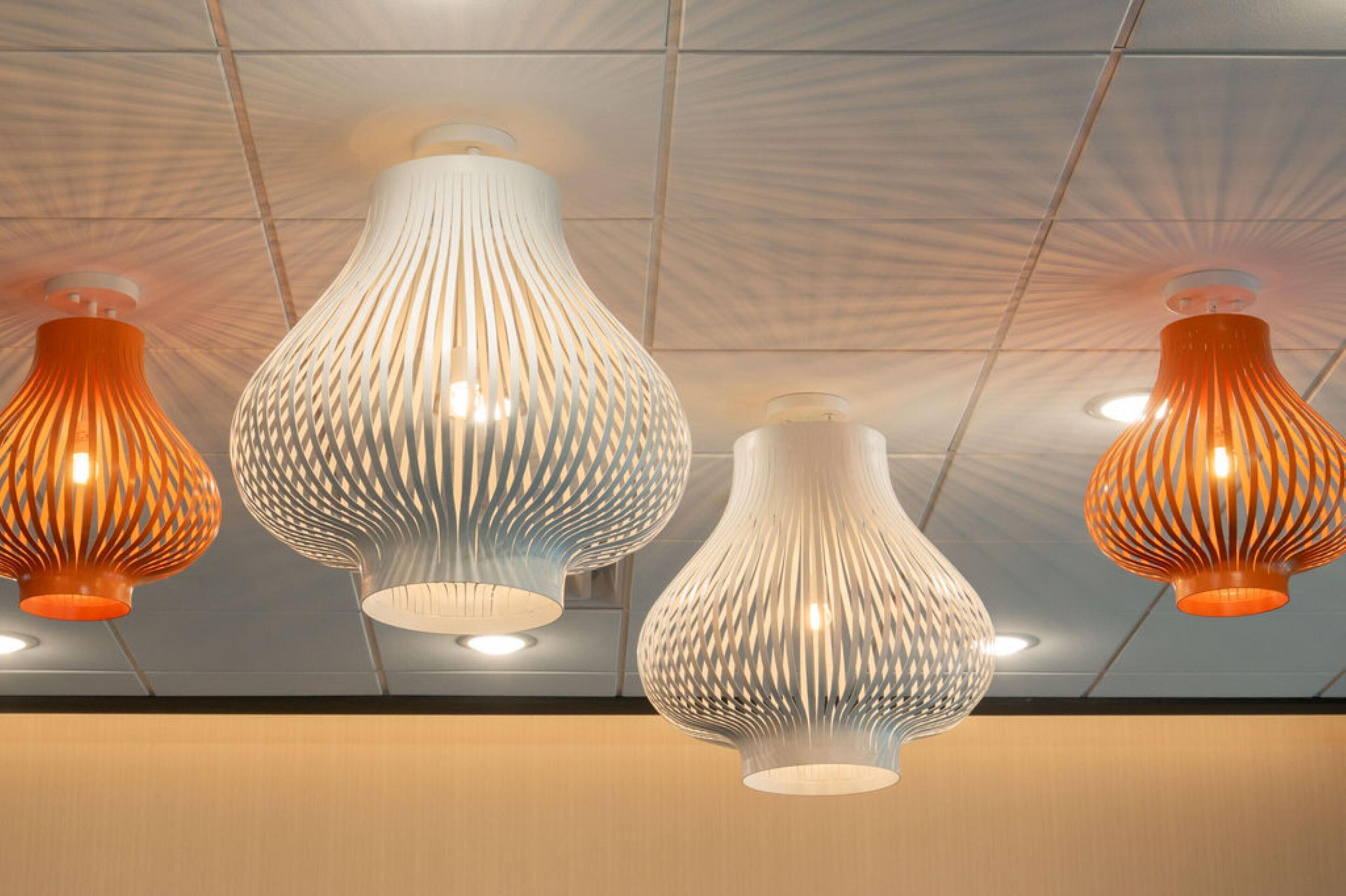 A ceiling with four pendant lights, two orange and two white, with a geometric pattern.