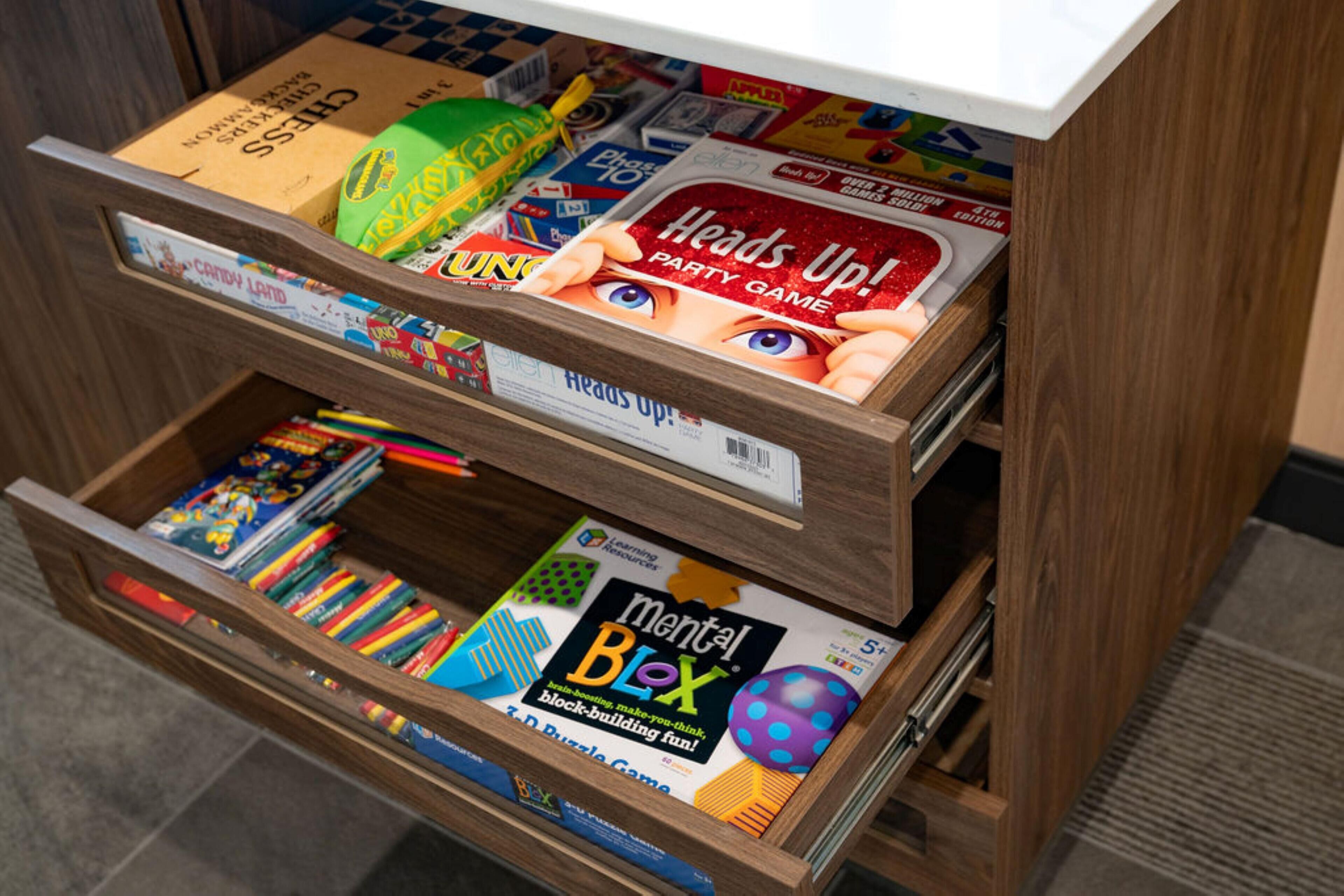 Un estante de madera con diversos juegos de mesa y rompecabezas, incluyendo 'Heads Up!' y 'Mental Blox'.