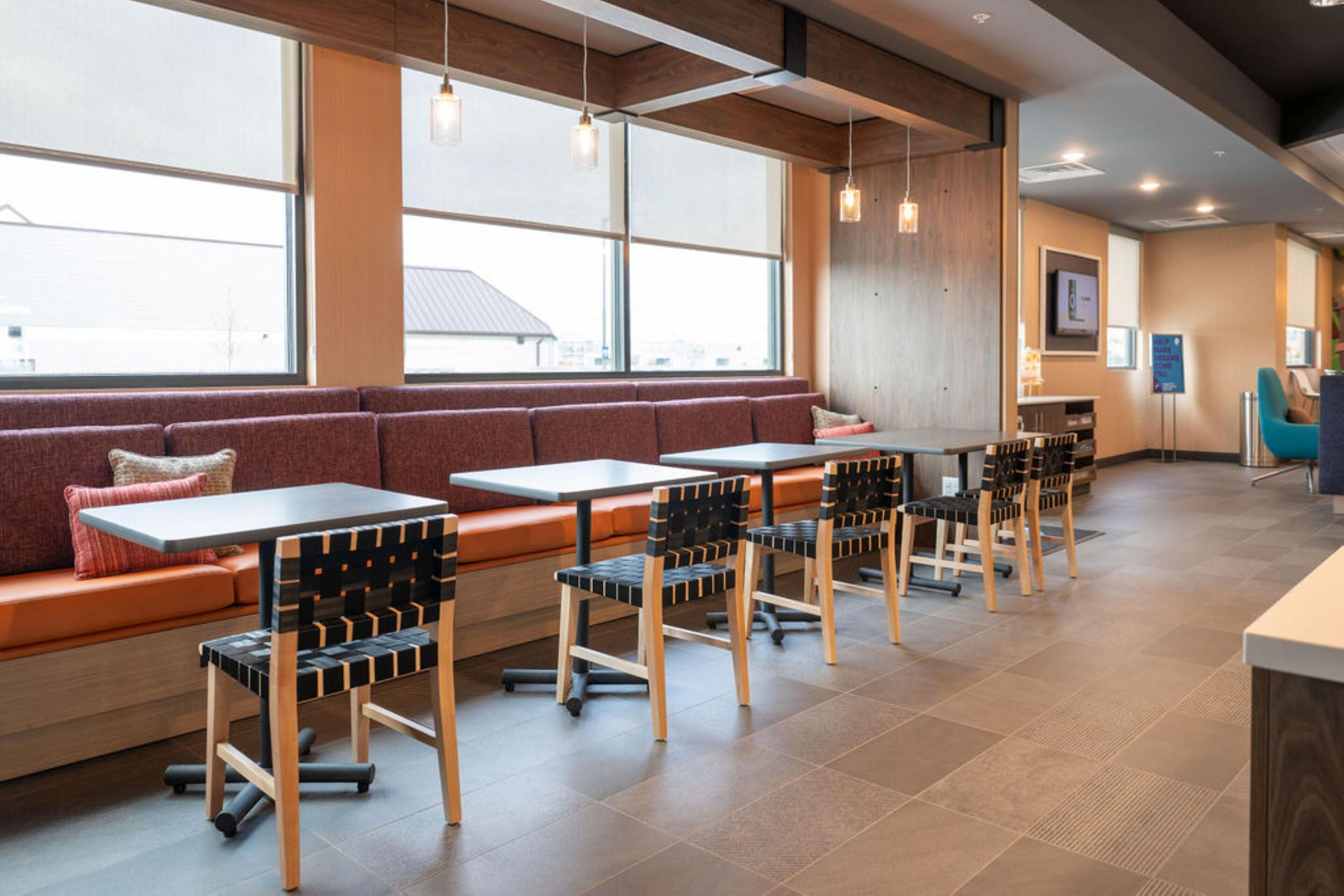 A modern restaurant interior with a long bench seating area, tables, and chairs.