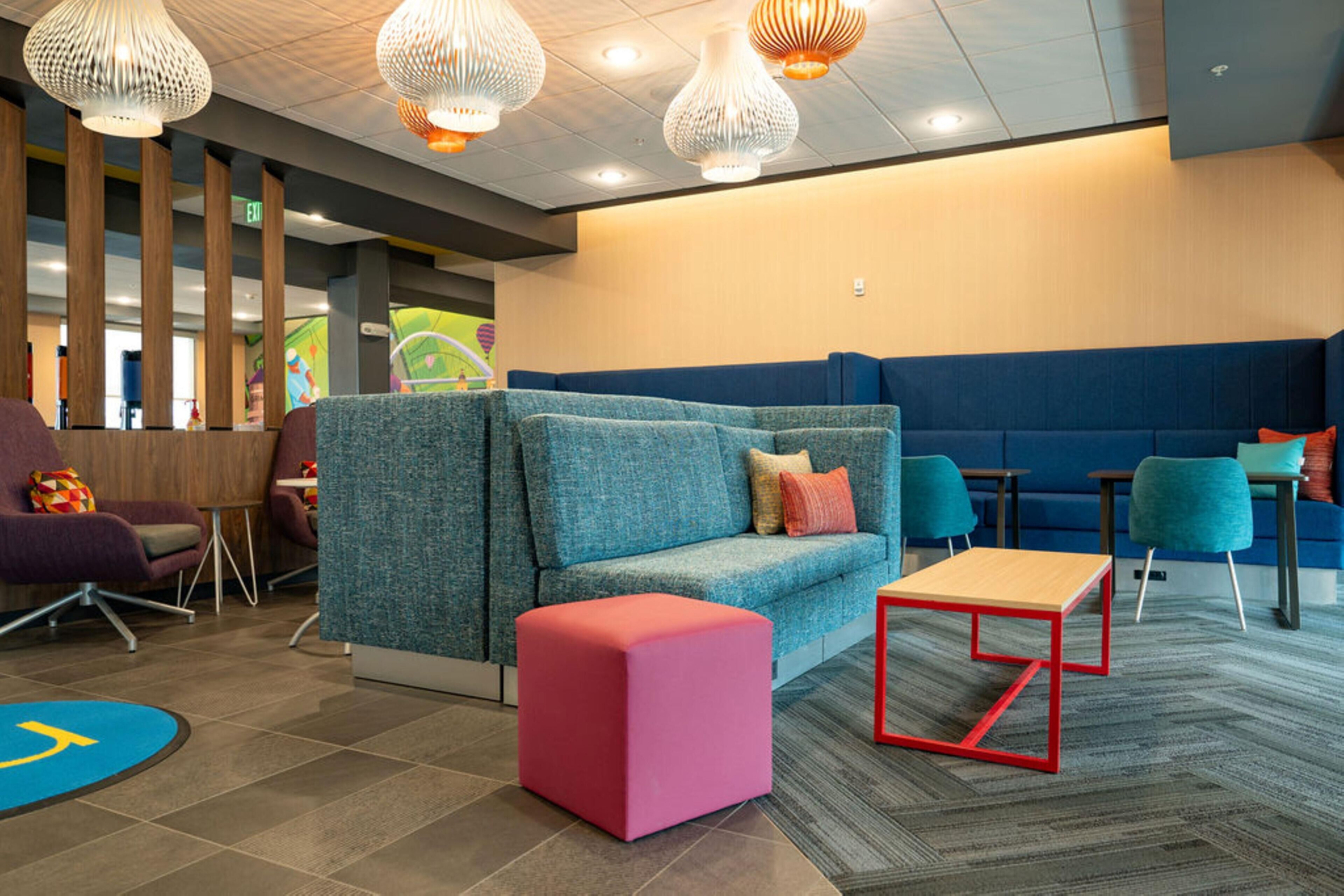 A modern waiting area with a blue sofa, a pink ottoman, and a red table.