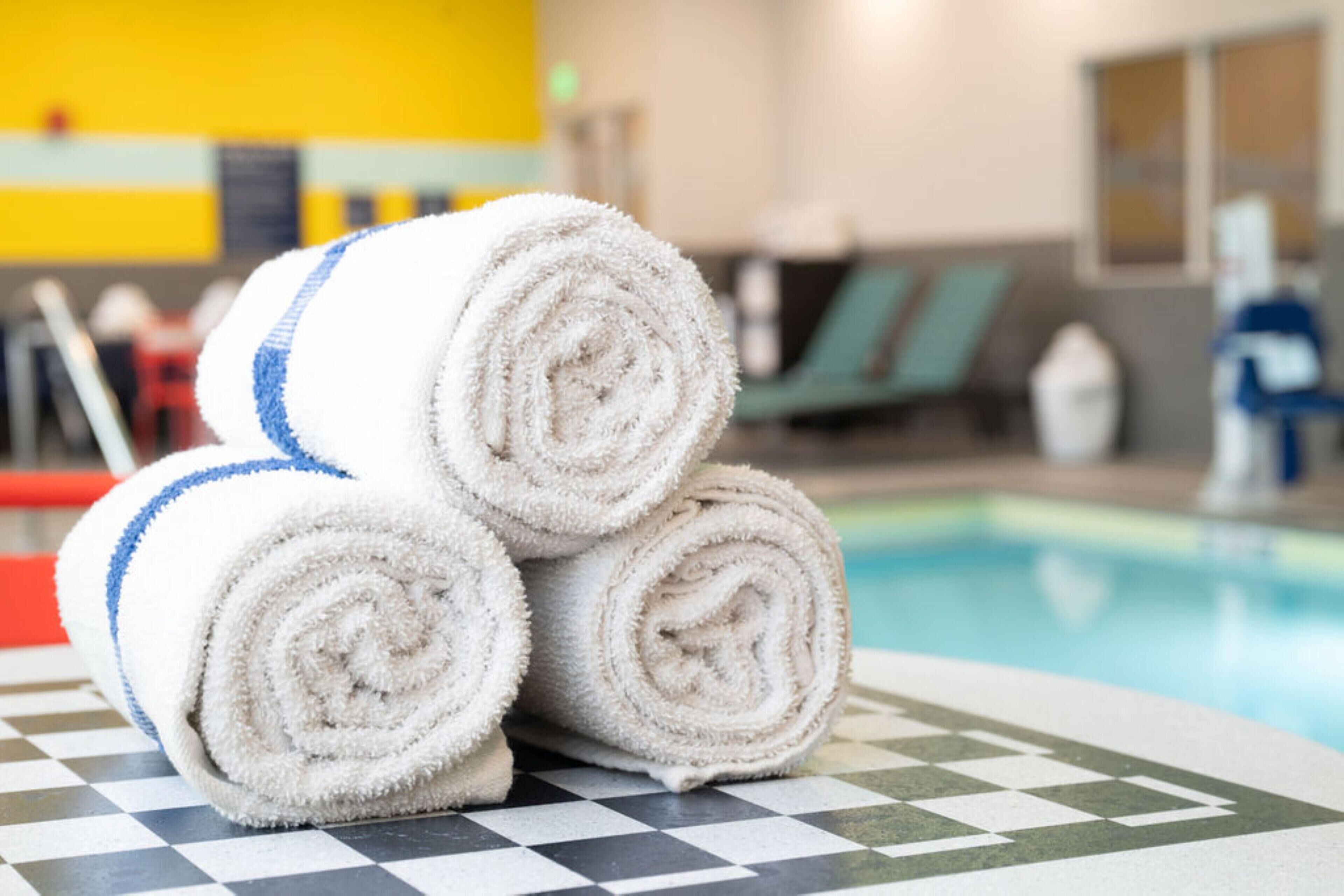 Une pile de serviettes enroulées est posée sur une table à carreaux, près d’un espace piscine.