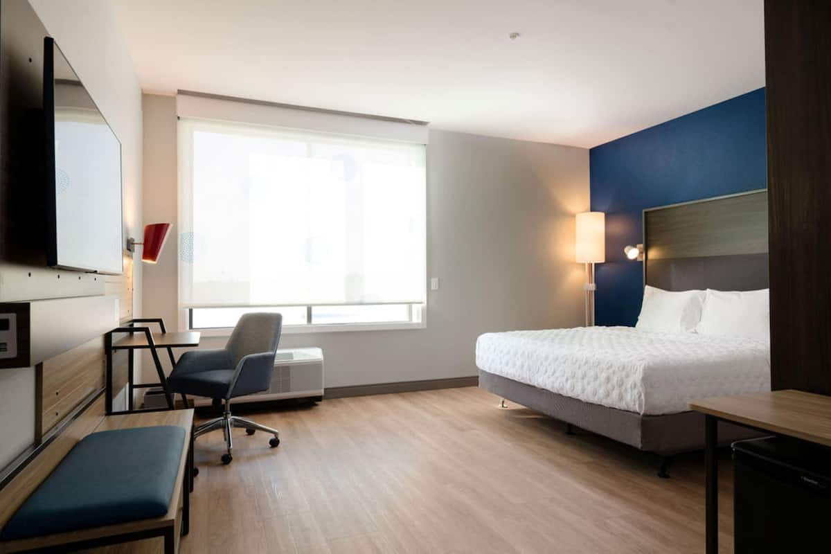Een hotelkamer met een bed, bureau, stoel, televisie en raam.