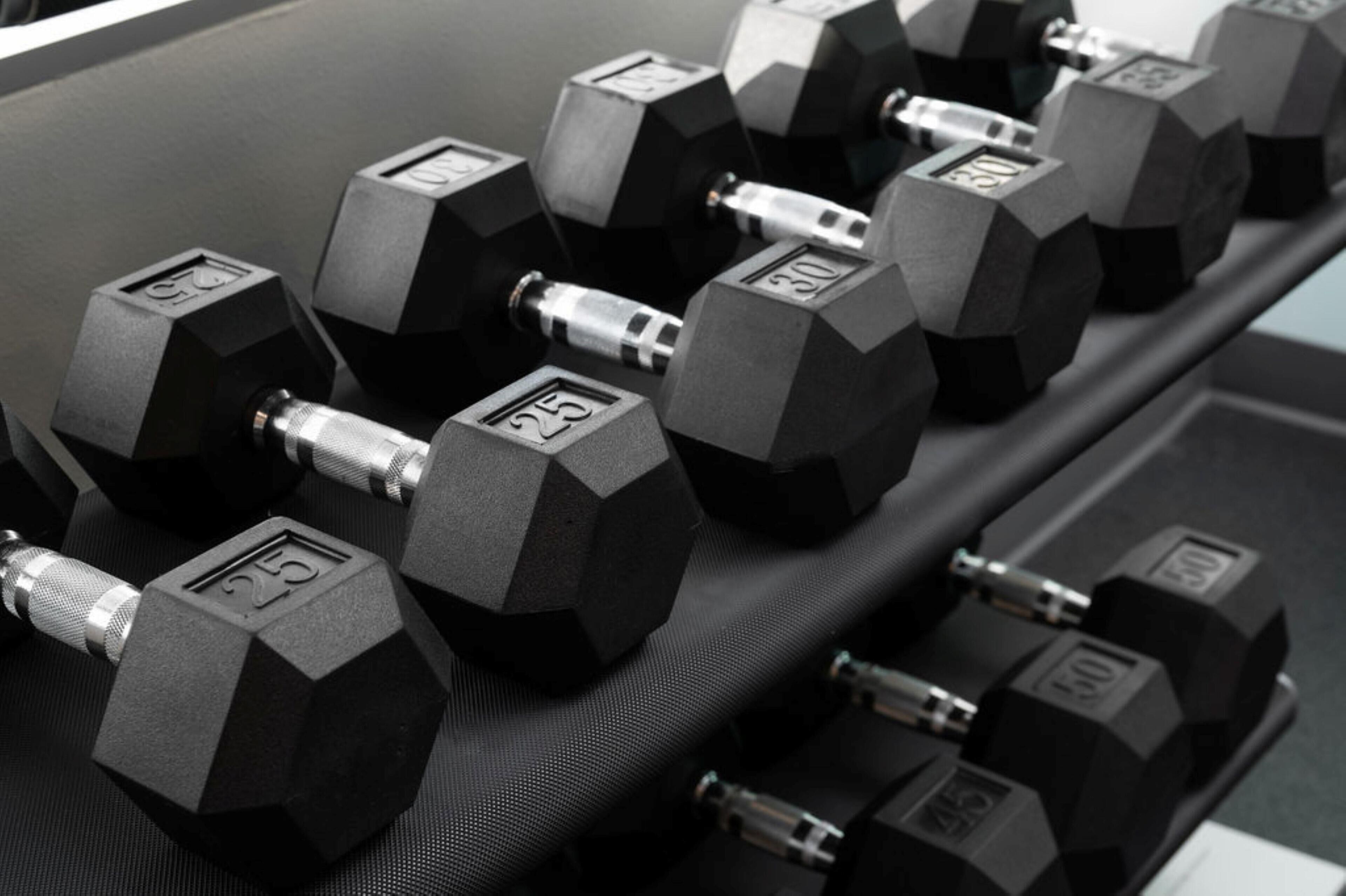 A set of hexagonal dumbbells with weight markings on a rack.
