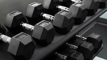A set of hexagonal dumbbells with weight markings on a rack.