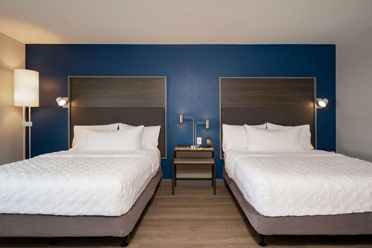 A hotel room with two beds, a nightstand, and a lamp.