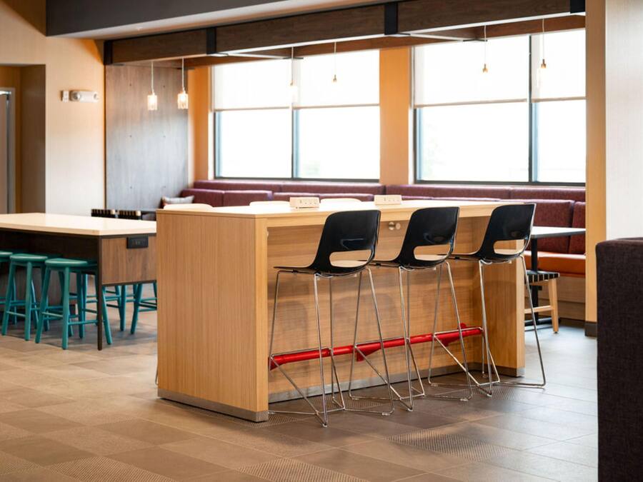 A modern restaurant with a wooden counter, black bar stools, and a seating area with red cushions.