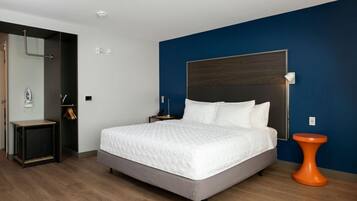 Une chambre d’hôtel moderne avec un grand lit, un plancher en bois, un mur d’accent bleu et une petite table d’appoint orange.