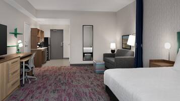 A hotel room with a bed, desk, chair, and a small kitchenette.