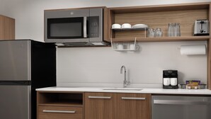 A modern kitchen with a stainless steel refrigerator, a microwave, a coffee maker, and wooden cabinets.