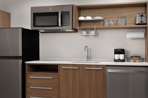 Una cocina moderna con un refrigerador de acero inoxidable, un microondas, una cafetera y armarios de madera.