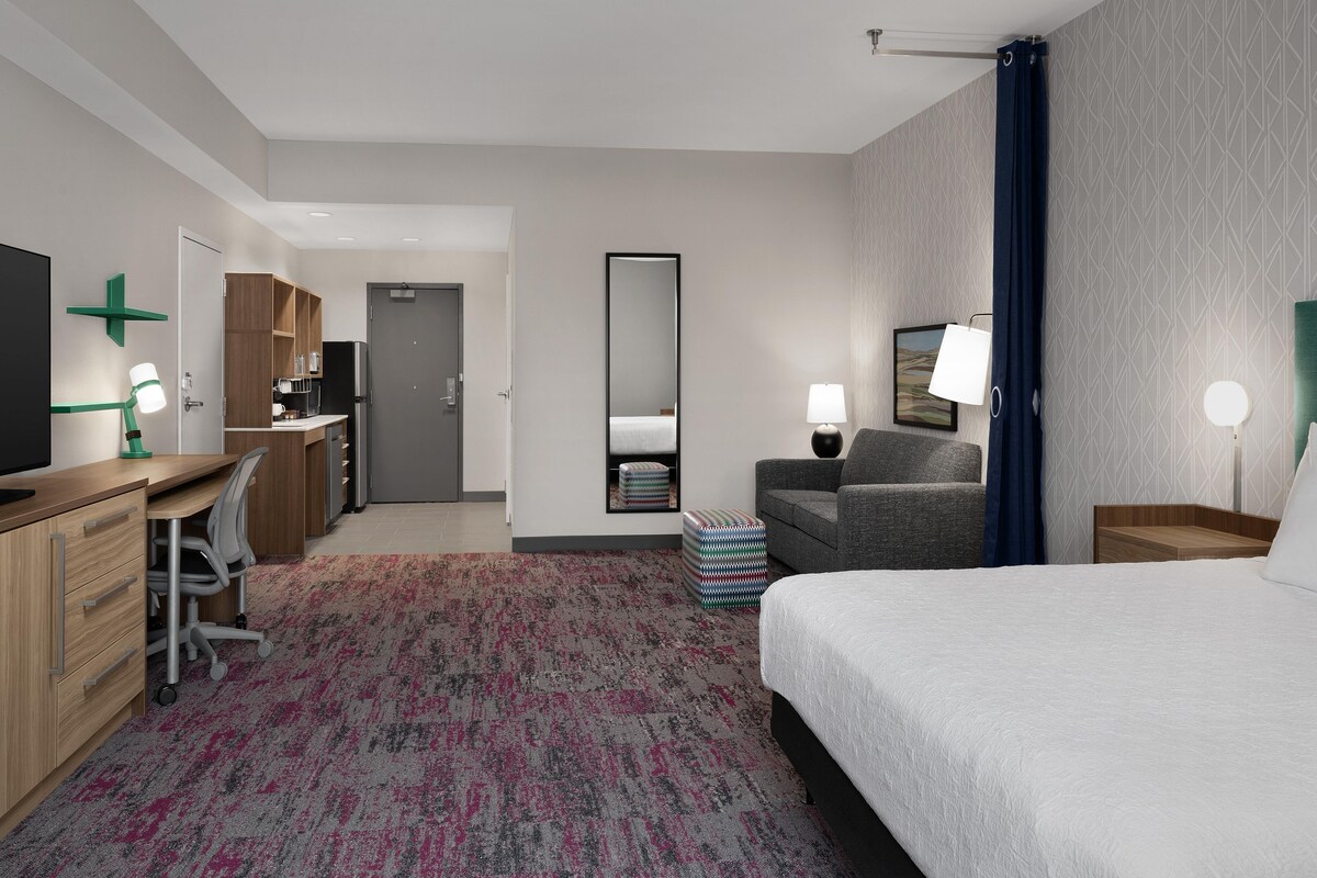 A hotel room with a bed, desk, chair, and a small kitchenette.