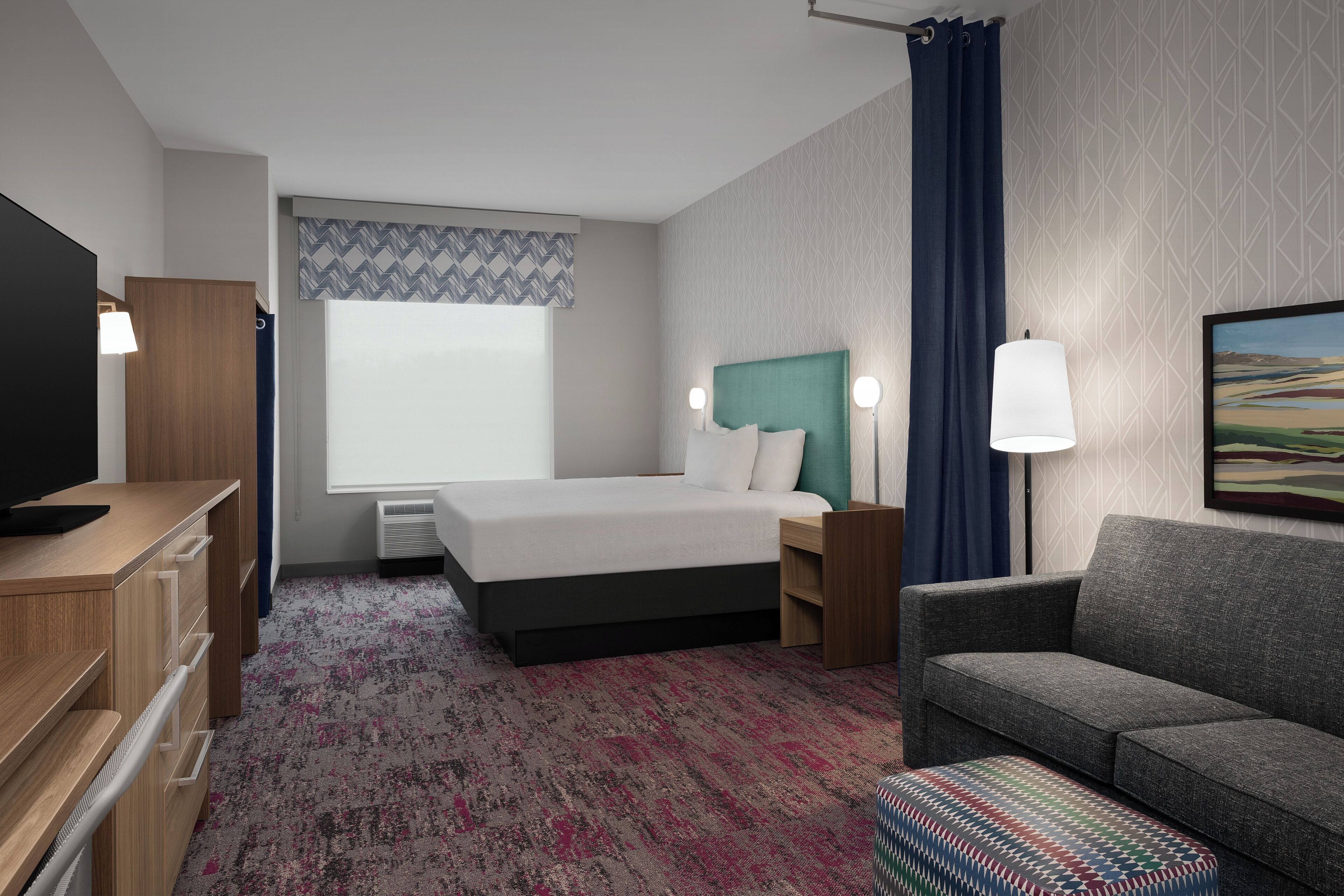 A hotel room with a bed, a desk, a TV, a sofa, and a painting on the wall.