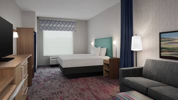 A hotel room with a bed, a desk, a TV, a sofa, and a painting on the wall.