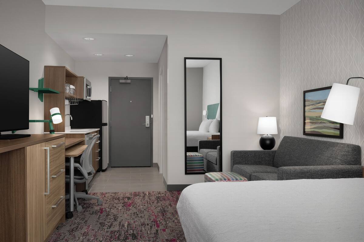 A hotel room with a bed, a desk with a computer, a chair, a TV, and a mirror.